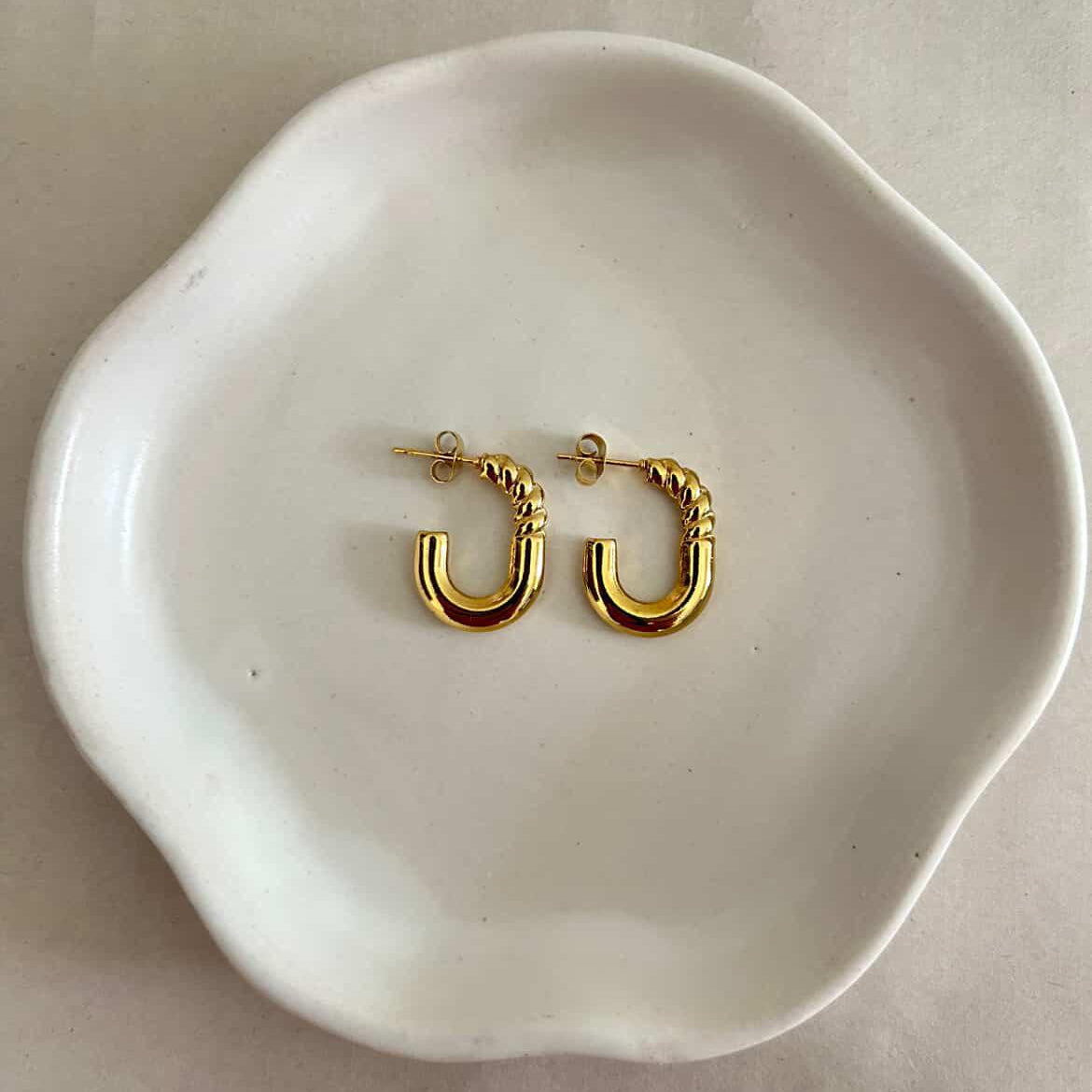 Gold hoop earrings on a white ceramic dish