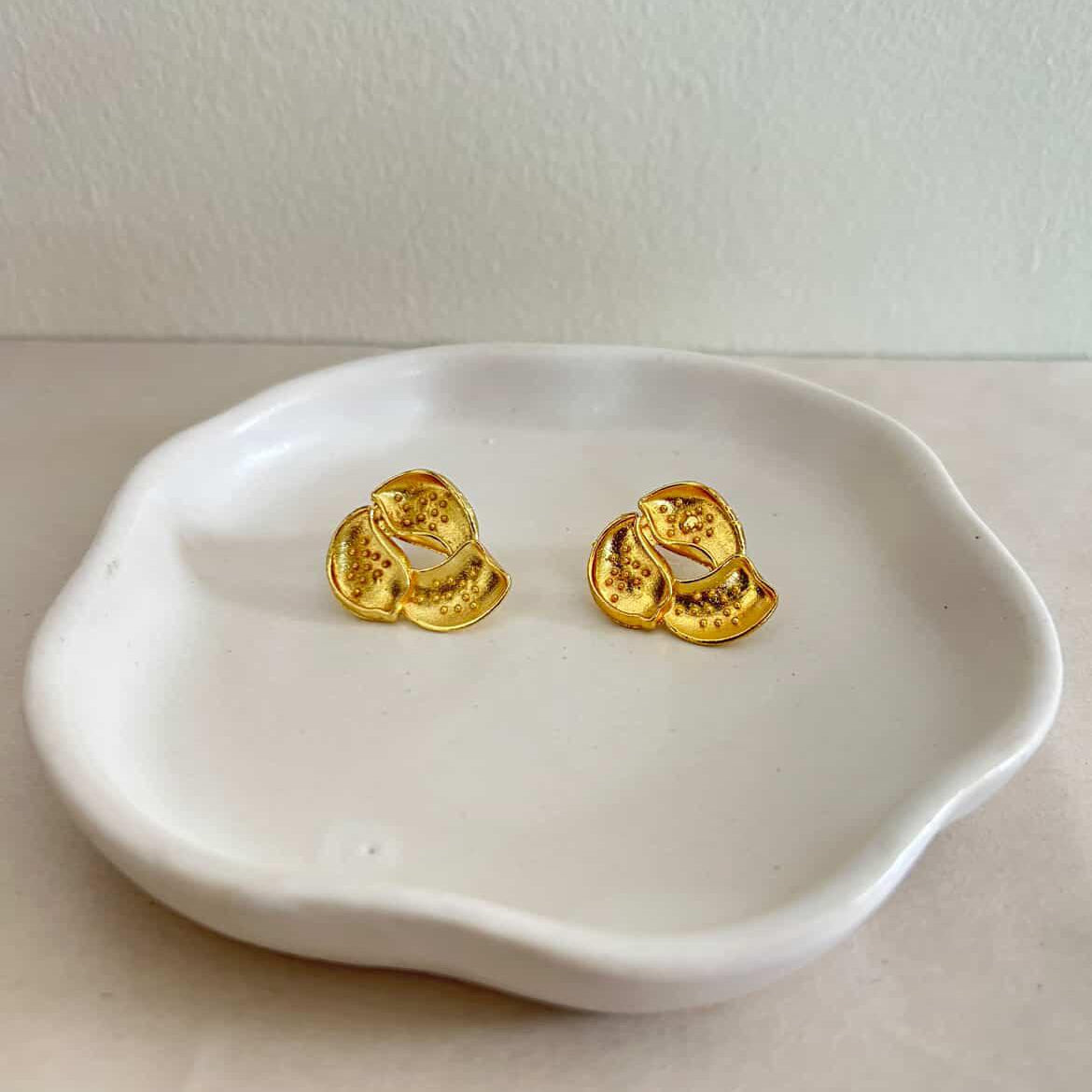 Gold earrings on a white dish with a plain background
