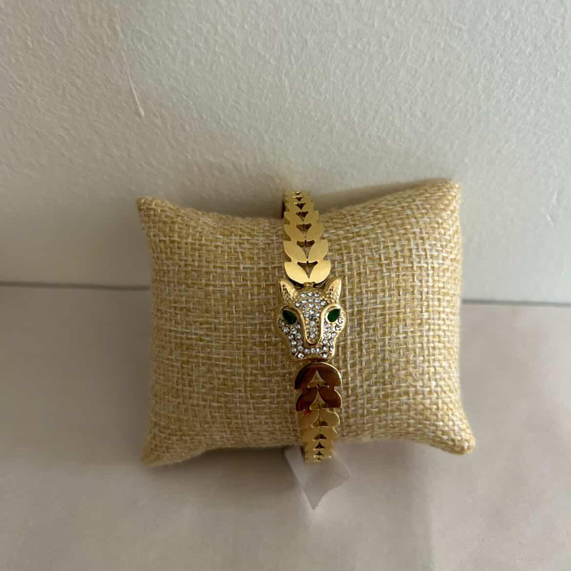Gold bracelet with a fox design on a beige pillow against a white background