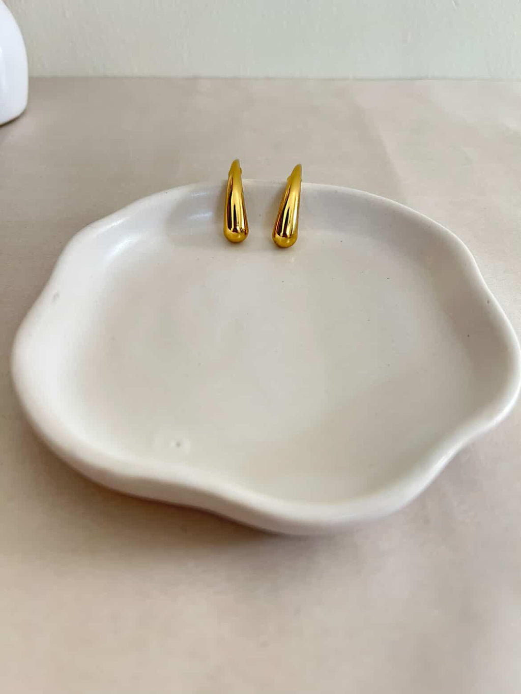 Gold earrings on a white ceramic dish with a plain background