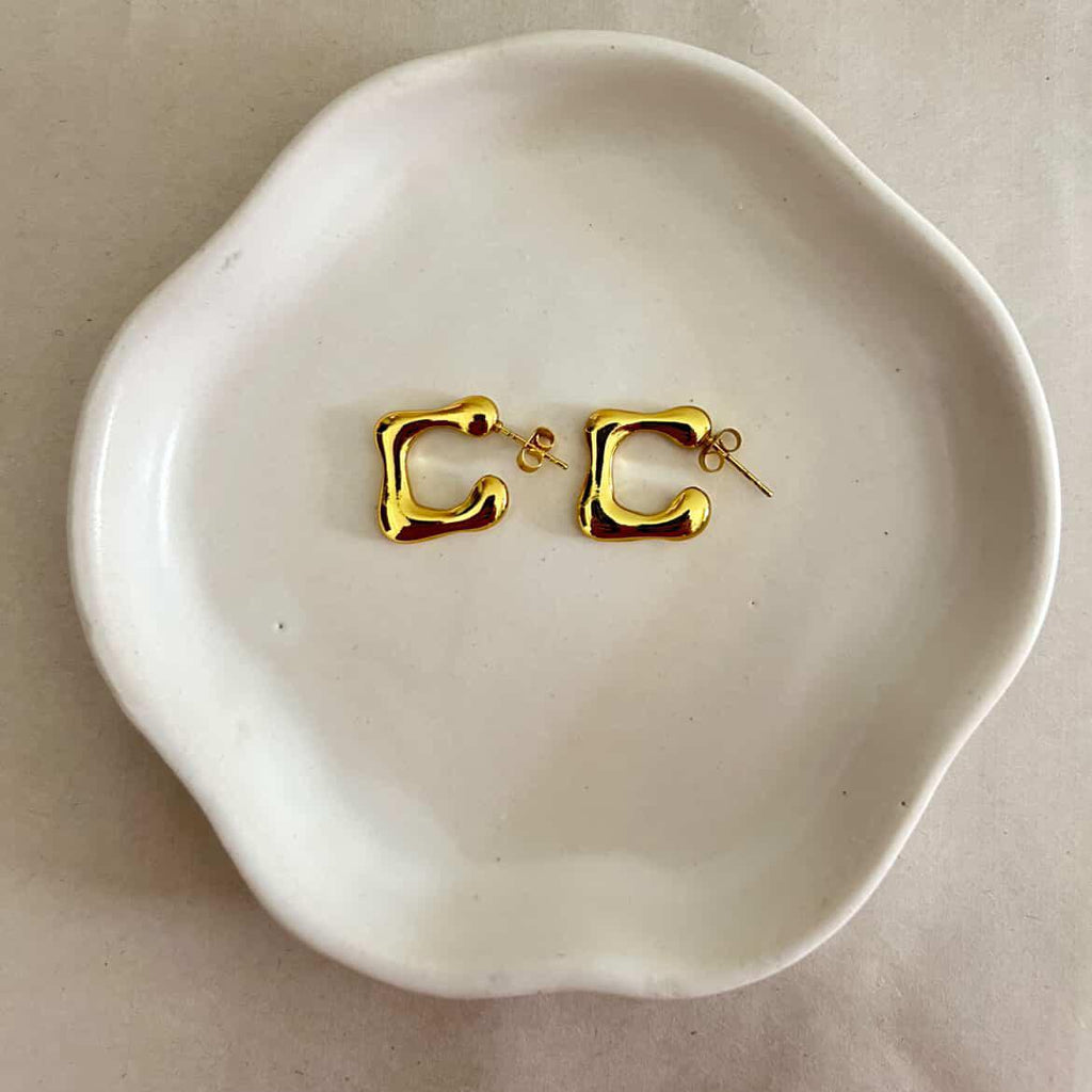 Gold earrings on a white dish with a beige background