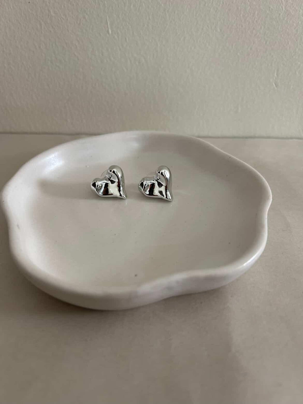 Silver dog-shaped earrings on a white dish against a plain background