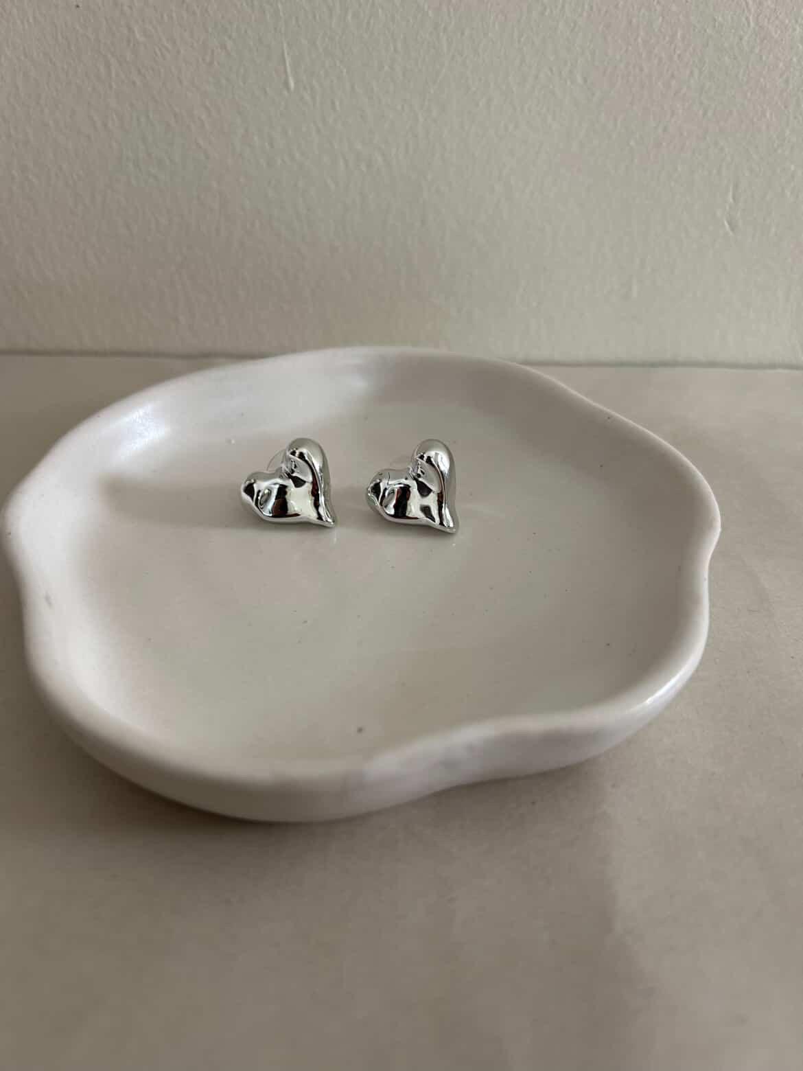 Silver dog-shaped earrings on a white dish against a plain background