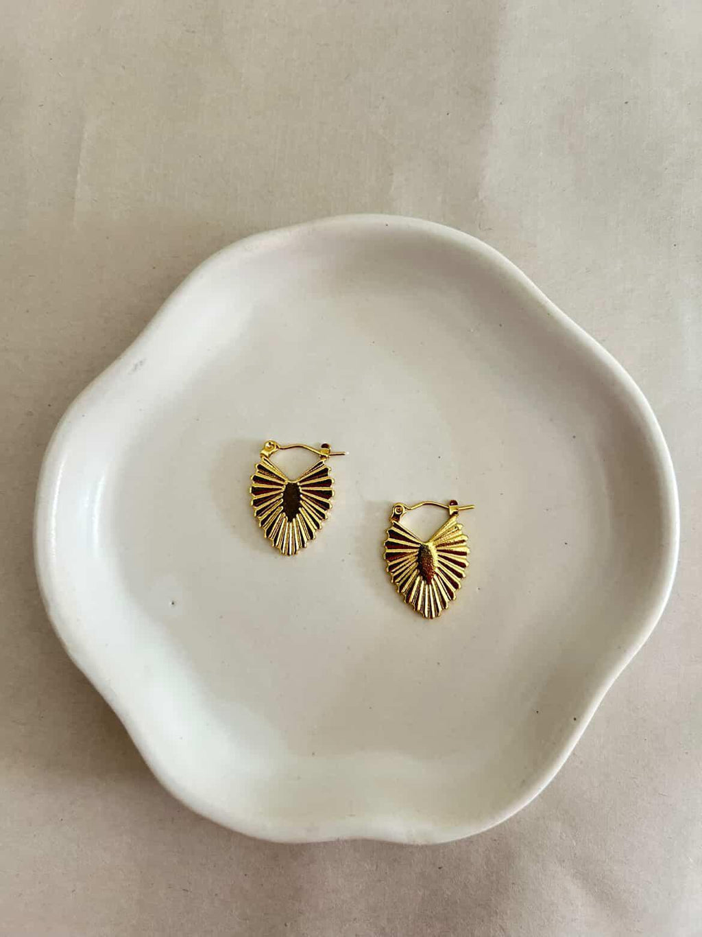 Gold hoop earrings on a white ceramic dish with a beige background